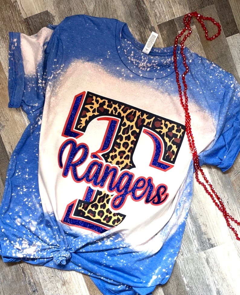 May include: A blue and white bleached t-shirt with a leopard print "T" and the word "Rangers" in blue glitter.
