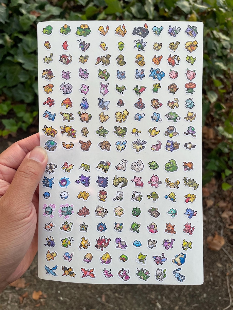 May include: A sheet of colorful, pixelated stickers featuring various cartoon creatures. The stickers are arranged in a grid pattern on a white background. The stickers are held by a hand.
