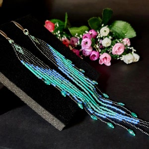 May include: A pair of long, beaded earrings with a cascading design. The earrings are made with black, blue, and green beads, and they have a silver-toned hook.