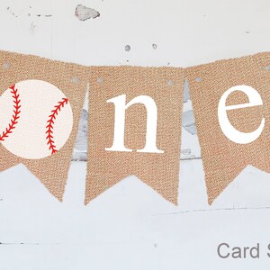 Puede incluir: Una pancarta de arpillera con la palabra "one" en letras blancas y una pelota de b&eacute;isbol roja y blanca en el lado izquierdo. La pancarta est&aacute; atada con un cordel y es perfecta para una fiesta de primer cumplea&ntilde;os.