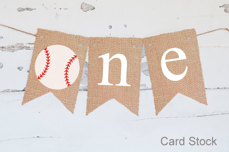 Puede incluir: Una pancarta de arpillera con la palabra "one" en letras blancas y una pelota de b&eacute;isbol roja y blanca en el lado izquierdo. La pancarta est&aacute; atada con un cordel y es perfecta para una fiesta de primer cumplea&ntilde;os.