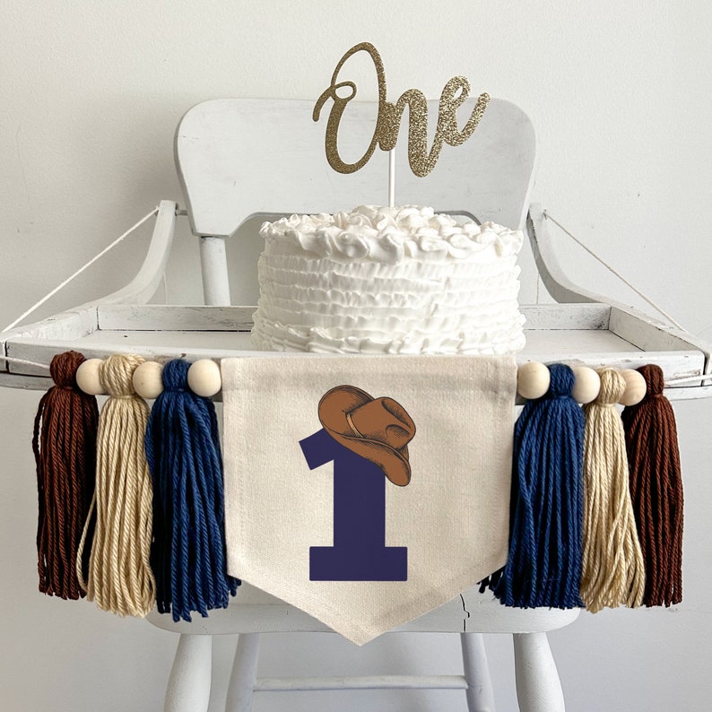 A 5 by 7 inch canvas center flag with a large navy blue number 1 topped with a brown cowboy hat. On each side there is a 5 inch navy blue, tan and brown yarn tassel, each separated by a wooden bead for a total of 6 tassels.