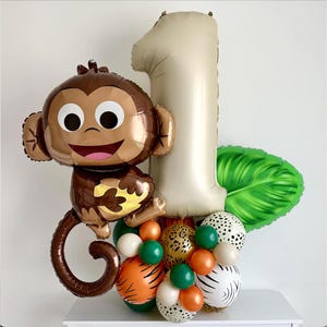 May include: A brown monkey balloon with a large number one balloon in beige, a green leaf balloon, and a cluster of smaller balloons in various colors and patterns, including orange, white, green, and brown.