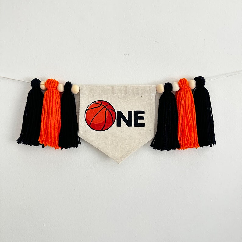 May include: A banner with black and orange tassels and a white fabric pennant with an orange basketball and the word "ONE" printed on it.