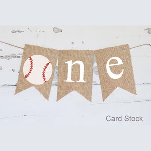Puede incluir: Una pancarta de arpillera con la palabra "one" en letras blancas y un gr&aacute;fico de b&eacute;isbol. La pancarta est&aacute; atada con un cordel y es perfecta para una fiesta de primer cumplea&ntilde;os.
