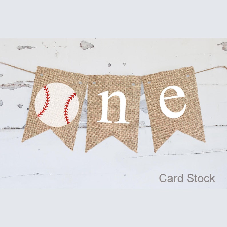 Puede incluir: Una pancarta de arpillera con la palabra "one" en letras blancas y un gr&aacute;fico de b&eacute;isbol. La pancarta est&aacute; atada con un cordel y es perfecta para una fiesta de primer cumplea&ntilde;os.