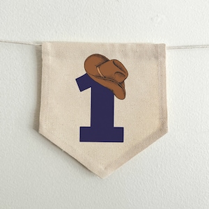 May include: A beige fabric pennant with a navy blue number "1" and a brown cowboy hat on top.