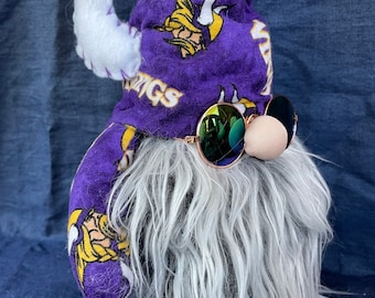 May include: A purple and yellow gnome with a white beard and a hat that says "Vikings". The gnome is wearing sunglasses.