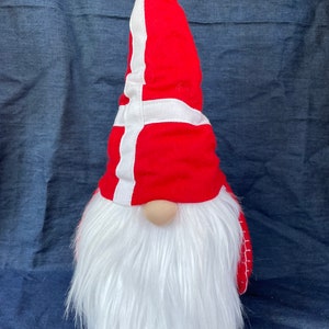 May include: A red and white gnome with a long white beard wearing a hat with the Danish flag on it.