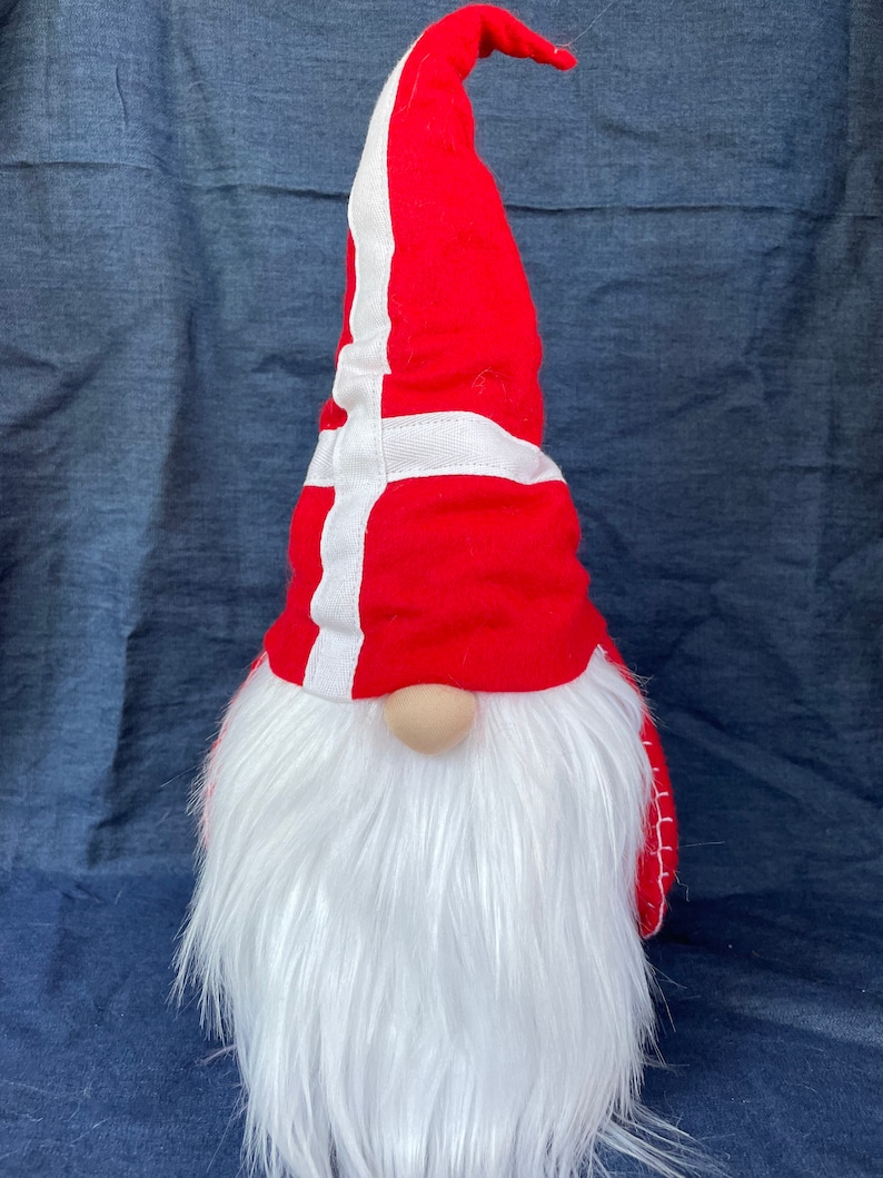 May include: A red and white gnome with a long white beard wearing a hat with the Danish flag on it.