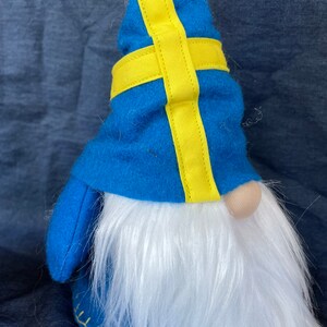 May include: A blue gnome with a white beard and a yellow and blue hat. The hat is decorated with a yellow cross, resembling the Swedish flag.