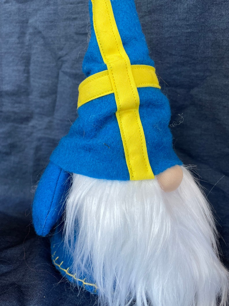 May include: A blue gnome with a white beard and a yellow and blue hat. The hat is decorated with a yellow cross, resembling the Swedish flag.
