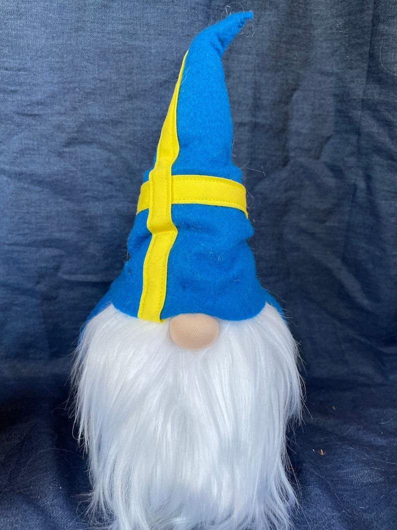May include: A blue gnome with a white beard and a blue and yellow hat. The hat has a yellow stripe that resembles the Swedish flag.