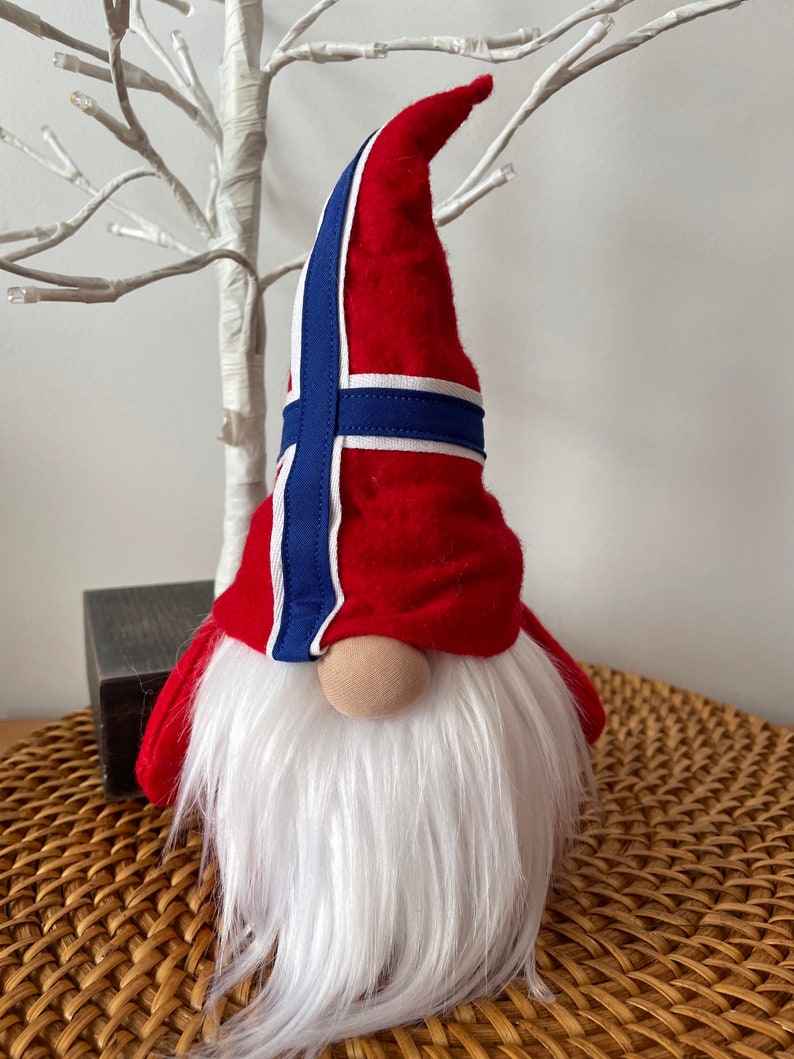 May include: A red and white gnome with a blue and white hat featuring the Norwegian flag. The gnome has a white beard and a red hat.