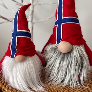 May include: Two gnomes with white beards and red hats decorated with the Norwegian flag. The gnomes are sitting on a woven wicker basket.