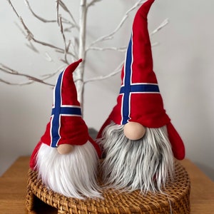 May include: Two plush gnomes with white beards and red hats decorated with the Norwegian flag. The gnomes are sitting on a woven wicker tray.