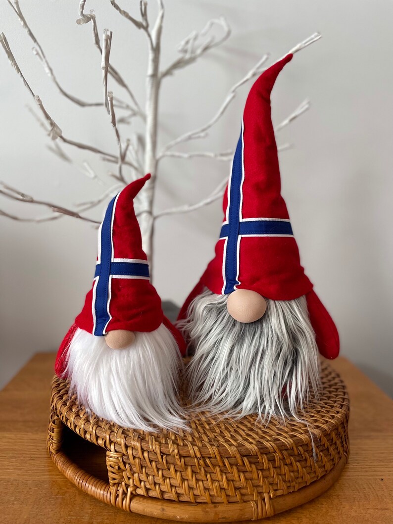 May include: Two plush gnomes with white beards and red hats decorated with the Norwegian flag. The gnomes are sitting on a woven wicker tray.