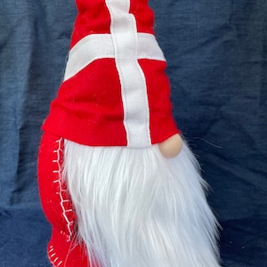 May include: A red and white gnome with a long white beard. The gnome's hat is decorated with the Danish flag.