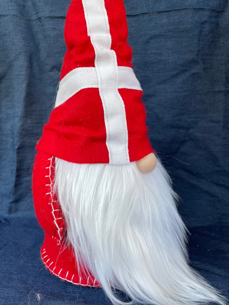 May include: A red and white gnome with a long white beard. The gnome's hat is decorated with the Danish flag.