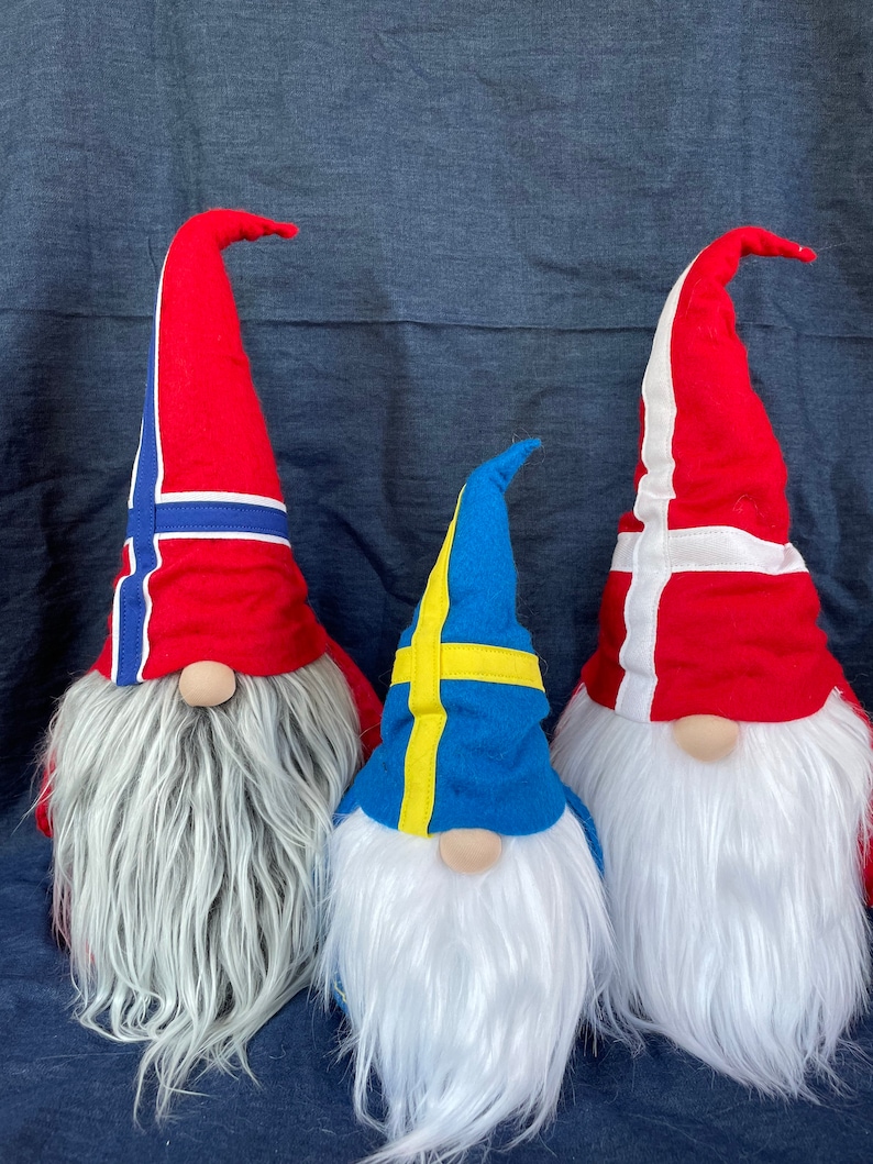 May include: Three gnomes wearing hats with the flags of Norway, Sweden, and Denmark. The gnomes are made of fabric and have white fur beards.