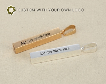 May include: Two rectangular pendants, one gold and one silver, with a loop for a chain. The gold pendant has the text "Add Your Words Here" and the silver pendant has the same text. The image also includes the text "CUSTOM WITH YOUR OWN LOGO".