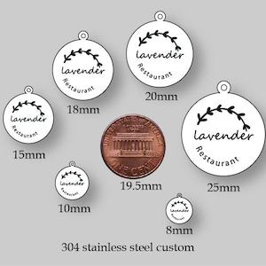 May include: A set of six round, white metal tags with a black floral design and the text "Lavender Restaurant". The tags are shown with a penny for size comparison. The tags are available in sizes 8mm, 10mm, 15mm, 18mm, 20mm, and 25mm.