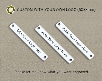 Op de afbeelding: Drie rechthoekige zilveren metalen labels met afgeronde hoeken en gaten aan de bovenkant. Elk label heeft de tekst "Add Your Logo Here" geschreven in zwarte, cursieve handschrift. De labels zijn 5 inch lang en 38 millimeter breed.