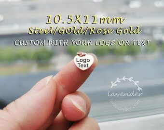 Op de afbeelding: Een kleine hartvormige bedel gemaakt van staal, goud of roségoud. De bedel is 10,5 mm bij 11 mm en kan worden gepersonaliseerd met een logo of tekst. De bedel wordt getoond op een vinger.