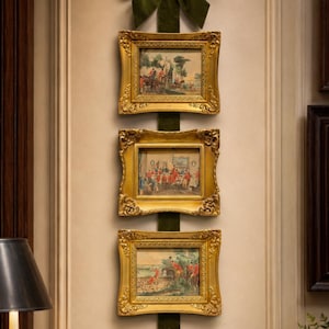 May include: A vertical wall hanging featuring three rectangular gold ornate frames suspended by a long dark green velvet ribbon topped with a large matching bow. Each frame contains a detailed print depicting a hunting scene with figures.