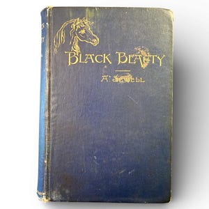 May include: A vintage hardcover book titled "Black Beauty" by A. Sewell. The book has a dark blue cover with gold lettering and a horse illustration. The book shows signs of wear, suggesting it is an antique.