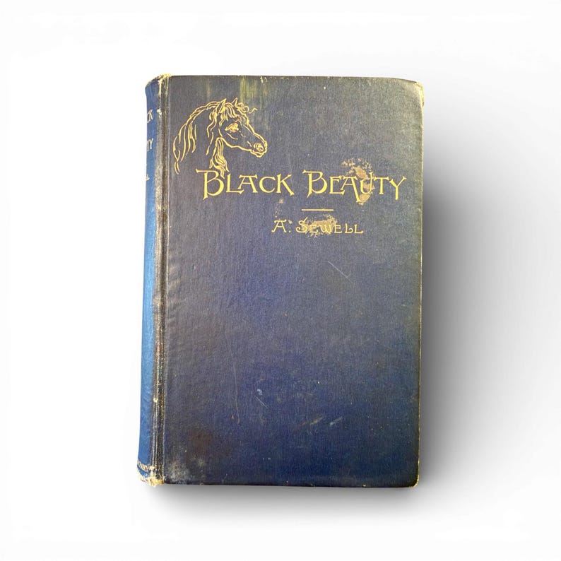 May include: A vintage hardcover book titled "Black Beauty" by A. Sewell. The book has a dark blue cover with gold lettering and a horse illustration. The book shows signs of wear, suggesting it is an antique.
