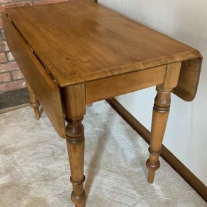 Op de afbeelding: Een lichtbruine houten klaptafel met gedraaide poten. De tafel heeft een rechthoekig blad met afgeronde hoeken en een klapblad aan één kant. De poten zijn ingewikkeld gesneden en de tafel lijkt van massief hout te zijn.