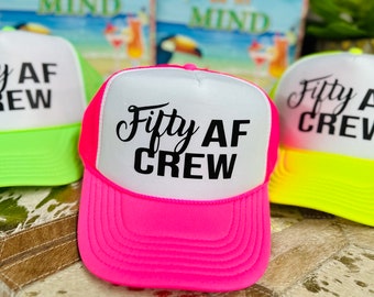 Puede incluir: Tres gorras de camionero de neón con redes blancas en la parte posterior y texto negro que dice "Fifty AF Crew". Las gorras son de color rosa, verde y amarillo.