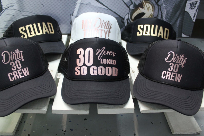 May include: Six black trucker hats with mesh back panels. The hats have different gold and rose gold lettering. The text on the hats reads "Squad", "My Dirty Thirty", "30 Never Looked So Good", "Dirty 30 Crew", and "Dirty 30 Crew".