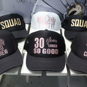 May include: Six black and white trucker hats with gold and rose gold lettering. The hats have different phrases on them, including "Dirty 30 Crew", "My Dirty Thirty!" and "30 Never Looked So Good".