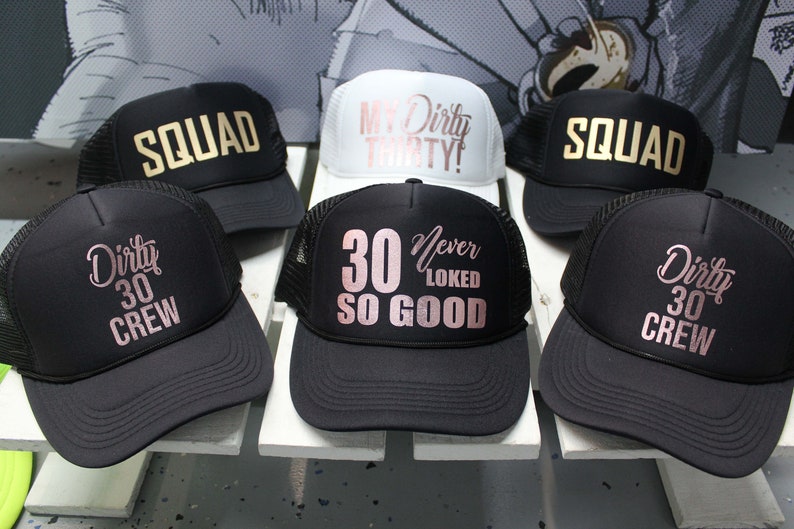May include: Six black and white trucker hats with gold and rose gold lettering. The hats have different phrases on them, including "Dirty 30 Crew", "My Dirty Thirty!" and "30 Never Looked So Good".