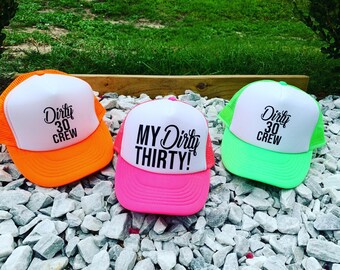 Puede incluir: Tres gorras de camionero con bordes de color neón. Las gorras son blancas con texto negro. Las gorras dicen "Dirty 30 Crew" y "My Dirty Thirty!"