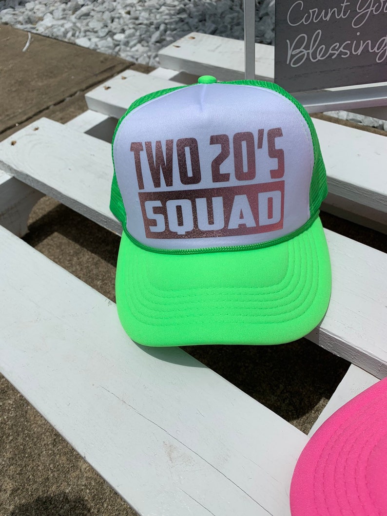 May include: A neon green and white trucker hat with the text "TWO 20'S SQUAD" in rose gold lettering.