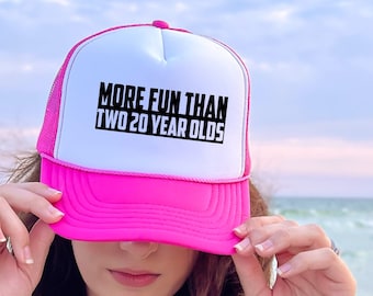 Puede incluir: Gorra de camionero rosa y blanca con texto negro que dice "More Fun Than Two 20 Year Olds".