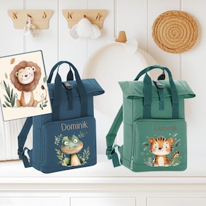 Op de afbeelding: Twee blauwe en groene kinderrugzakken met een roll-top sluiting. De rugzakken hebben een gepersonaliseerd naamschild met de tekst "Dominik". Eén rugzak heeft een groene kikker en de andere een tijger.