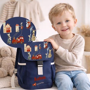 Può includere: Zaino blu navy con chiusura a patta e dettagli bianchi. La patta presenta un design stravagante di una caserma dei pompieri, un'autopompa e un elicottero con personaggi dei cartoni animati. Il nome "Anton" è stampato.