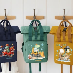 Può includere: Tre zaini personalizzati blu navy, verdi e giallo senape, ognuno con una grafica di dinosauro unica. Lo zaino blu navy presenta un dinosauro pompiere, quello verde un operaio edile e quello giallo un pirata. Ogni borsa ha il nome "Dominik".