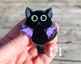 以下が含まれることがあります： 紫色の羽根と緑色の目をした黒い猫。猫はレジン製で、キラキラとした仕上げになっています。可愛くて幻想的なチャームです。