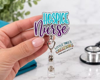 May include: A badge reel featuring a silver glitter acrylic topper with the text Hospice Nurse in teal and purple script. The topper is attached to a clear plastic retractable cord mechanism with a metal clip and a clear vinyl strap for an ID badge.