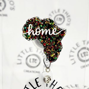 May include: A black and green glitter filled outline of the continent of Africa with the word "home" written in white cursive. The outline is attached to a clear plastic retractable badge holder.