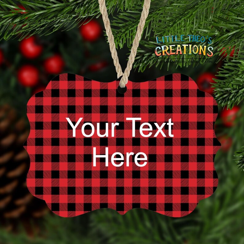 Puede incluir: Adorno navide&ntilde;o a cuadros rojos y negros con el texto "Your Text Here" en blanco. El adorno est&aacute; colgado de una cuerda de hilo natural. El fondo incluye agujas de pino y bayas rojas.