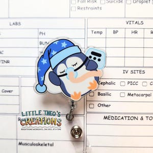May include: A penguin-themed badge reel featuring a sleeping penguin wearing a blue nightcap with white stars. The penguin is holding a medical device. The reel has the text "LITTLE THEO'S CREATIONS" and "BRIGHTENING WORKDAYS, ONE REEL AT A TIME".