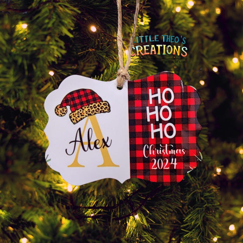 Puede incluir: Un adorno navide&ntilde;o con un dise&ntilde;o festivo. El adorno presenta un patr&oacute;n de cuadros de b&uacute;falo rojo y negro y las palabras "Ho Ho Ho Christmas 2024". El otro lado tiene un gorro de Pap&aacute; Noel y el nombre "Alex".