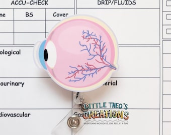 Pode incluir: Um porta-crachá de anatomia ocular rosa e branco com um cordão retrátil de plástico transparente. O porta-crachá tem o texto "DITTLE THEO'S Creations" e "BRIGHTENING WORKDAYS, ONE REEL AT A TIME". O fundo é um gráfico médico branco.