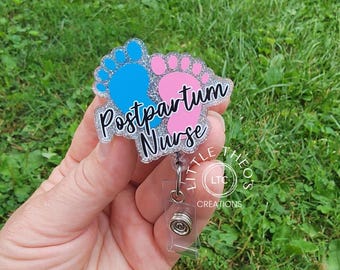 May include: A silver glitter badge holder with a blue and pink footprint design and the text "Postpartum Nurse". The badge holder has a clear plastic retractable reel.